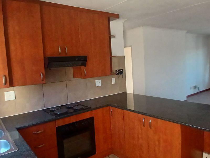Open-plan kitchen featuring wooden cabinetry, granite countertops, and integrated appliances, flowing into a spacious living area with access to a balcony.