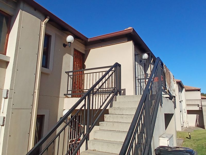 Exterior view of a townhouse complex featuring a concrete staircase, metal railings, and entrance doors with visible wear to the exterior wall finishes.