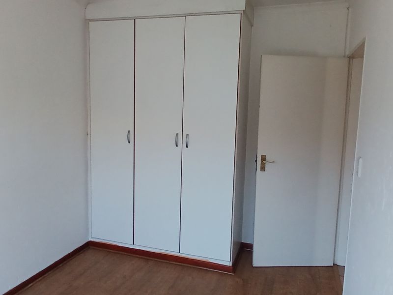 A clean, empty bedroom featuring neutral walls, laminate flooring, and built-in cupboards, offering a blank canvas for personalization.