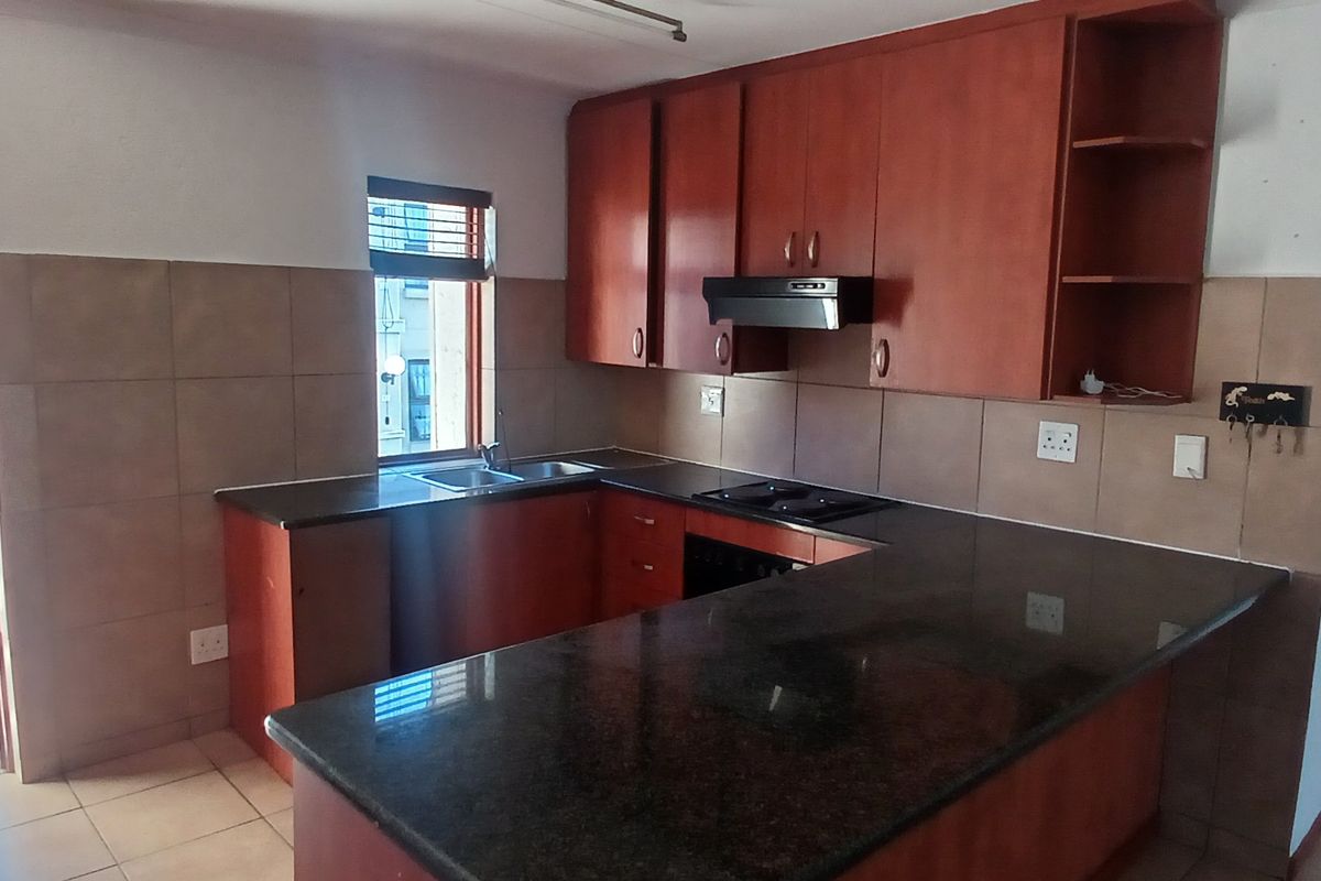 Functional kitchen featuring dark wood cabinetry, granite countertops, integrated hob, extractor fan, and direct access to an outdoor balcony area.