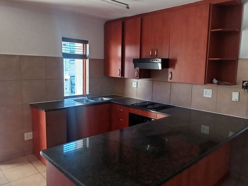 Functional kitchen featuring dark wood cabinetry, granite countertops, integrated hob, extractor fan, and direct access to an outdoor balcony area.