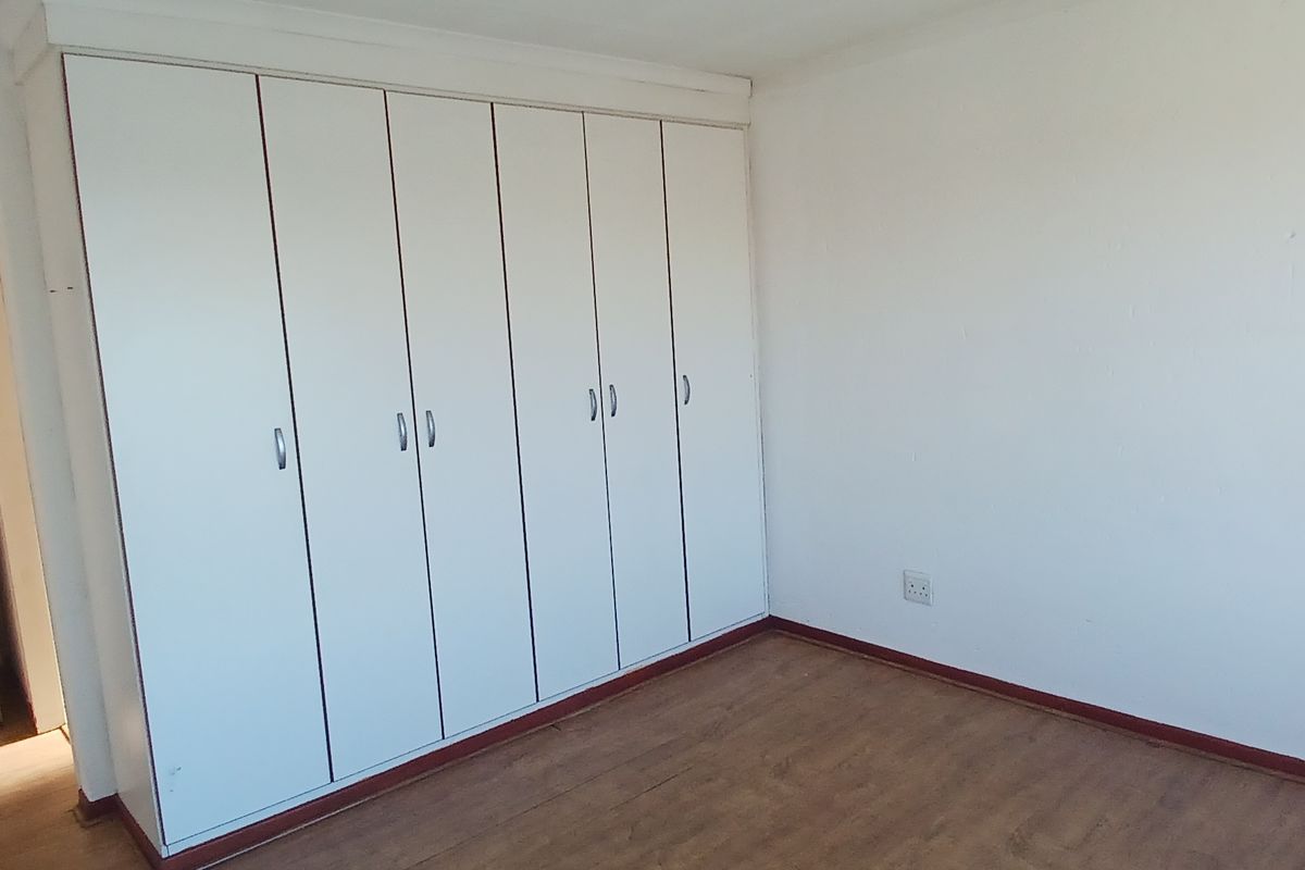 A vacant bedroom featuring extensive built-in cupboards, laminate flooring, and neutral wall finishes, offering a clean canvas for personalization.