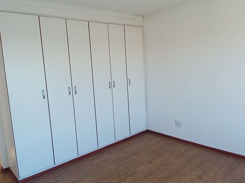 A vacant bedroom featuring extensive built-in cupboards, laminate flooring, and neutral wall finishes, offering a clean canvas for personalization.