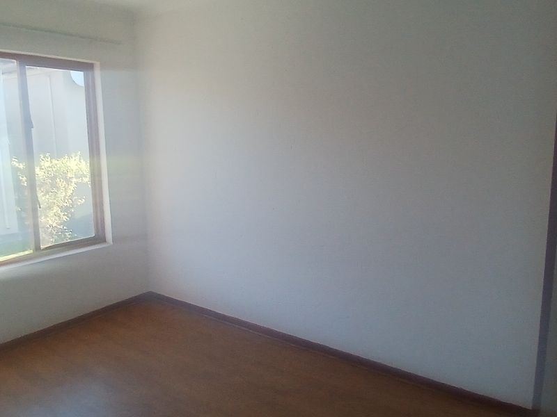 A bright, empty bedroom featuring laminate flooring and a large window, providing a blank canvas for personalization.