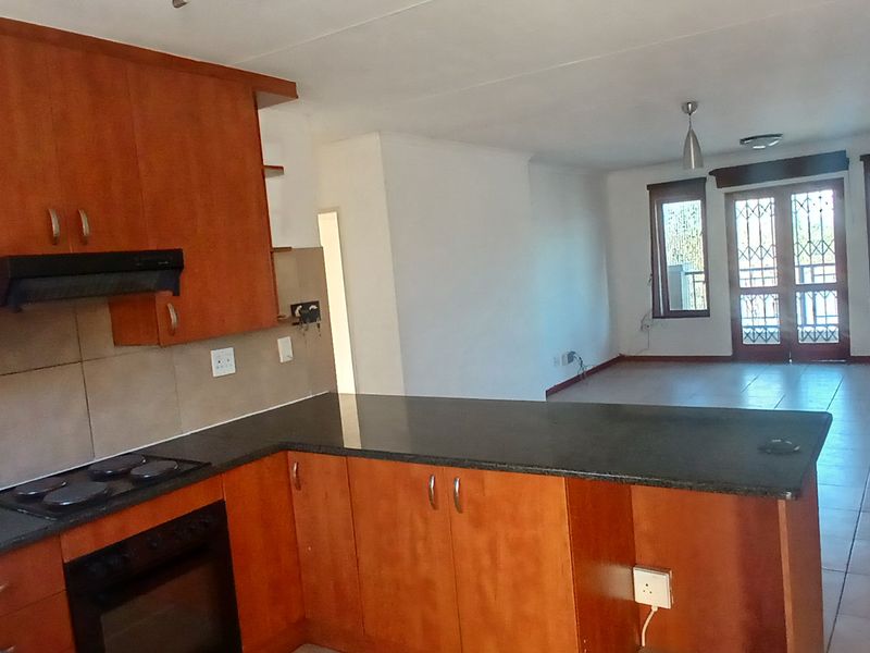 Open-plan living area featuring a kitchen with wood-finish cabinetry, granite countertops, and integrated appliances, flowing into a spacious living room with tiled floors.