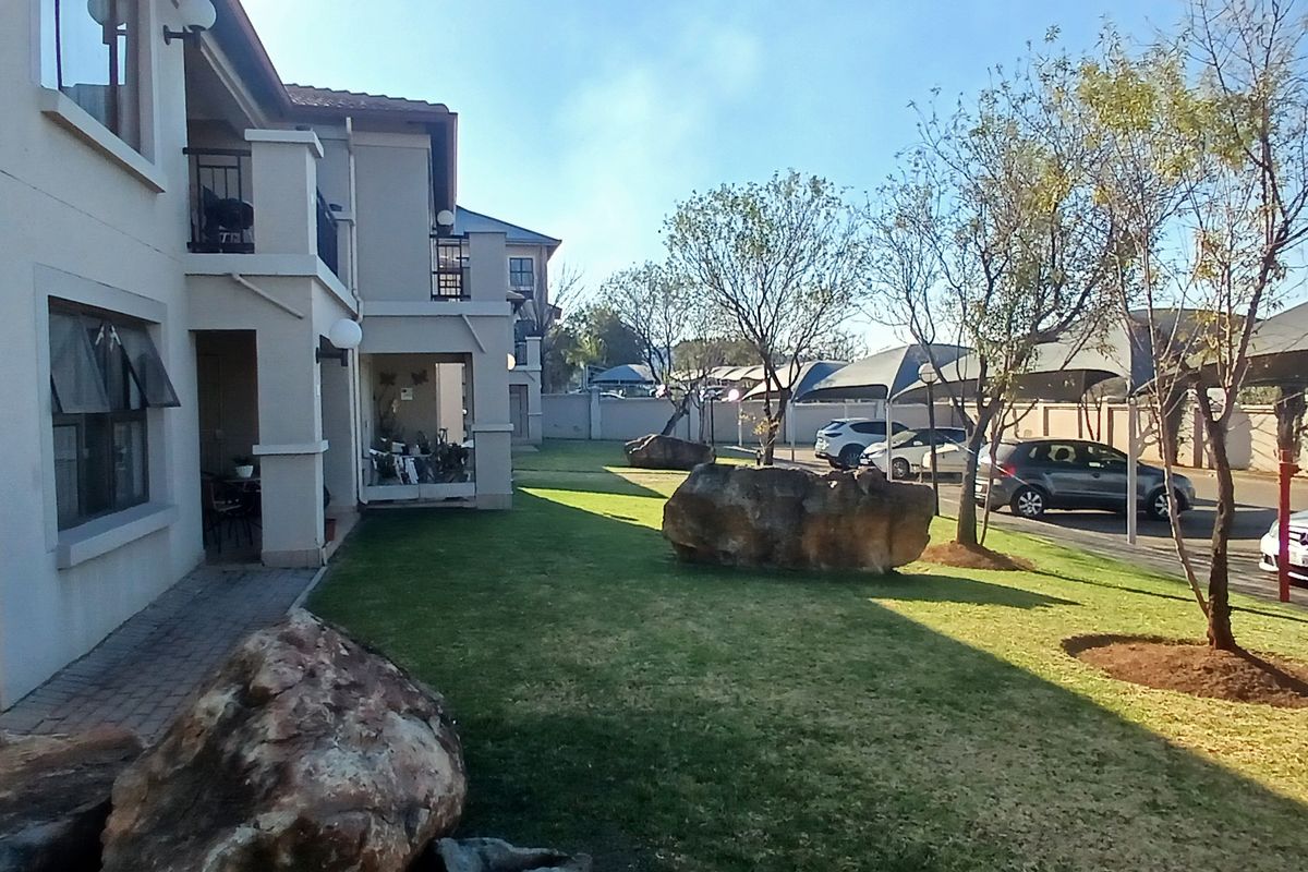 Exterior view of the townhouse complex featuring a well-maintained garden, paved walkways, and covered parking bays.