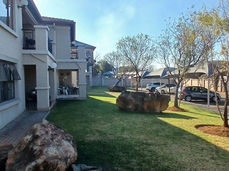 Exterior view of the townhouse complex featuring a well-maintained garden, paved walkways, and covered parking bays.