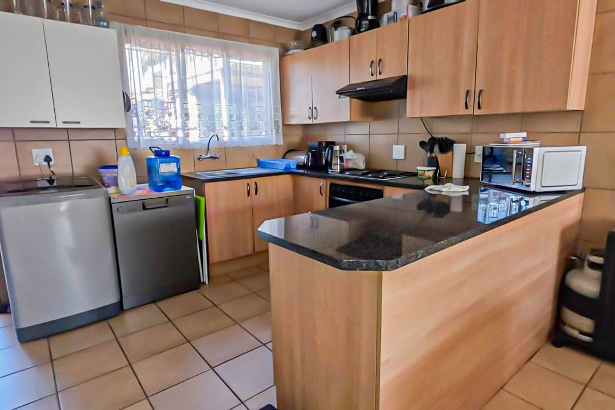 Functional kitchen featuring laminate cabinetry, granite countertops, built-in oven, hob, extractor fan, and tiled finishes with direct access to an outdoor area.