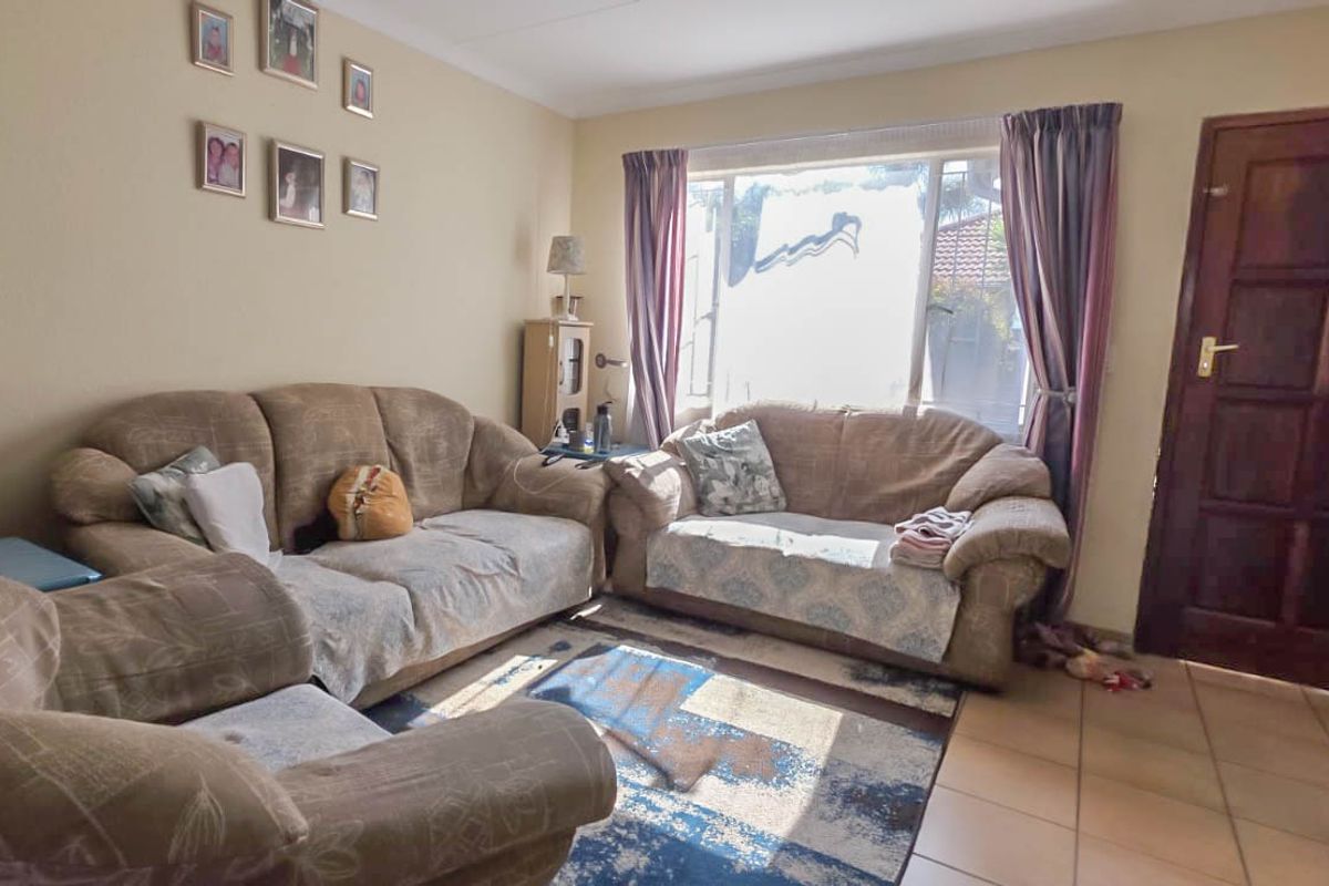 A functional living room featuring tiled flooring, a large window for natural light, and a traditional timber panelled entrance door.