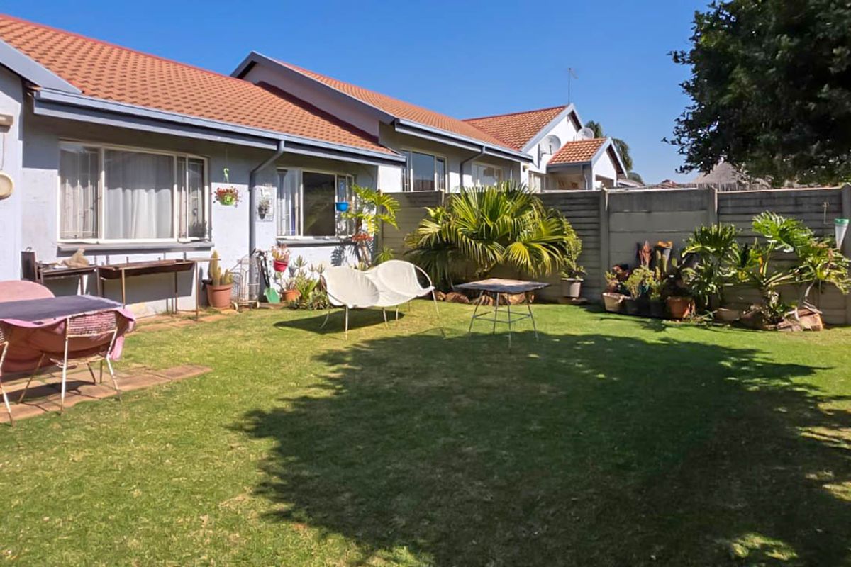 A private rear garden featuring a well-maintained lawn, paved patio area, and secure concrete boundary wall, offering a pleasant outdoor space for the townhouse.