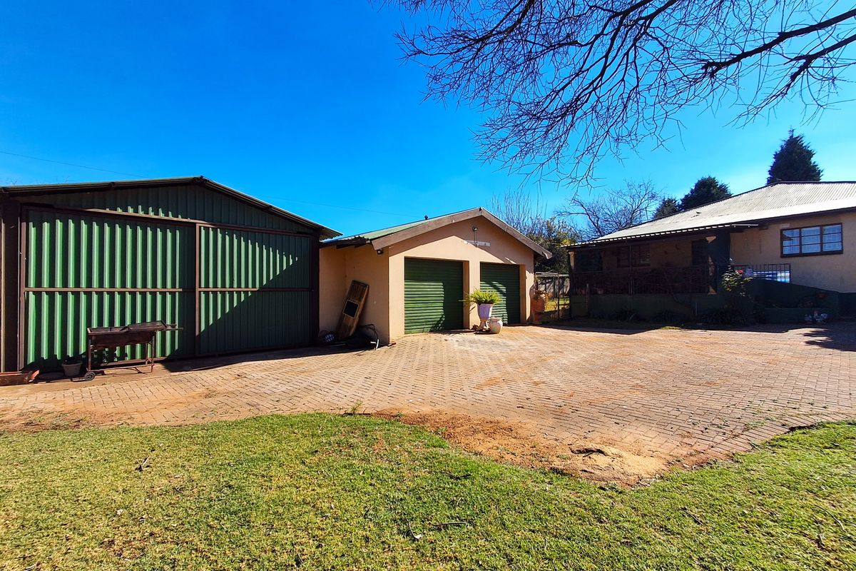 Rear exterior view featuring a paved driveway, a double garage, and a large corrugated metal storage shed set against a clear blue sky.