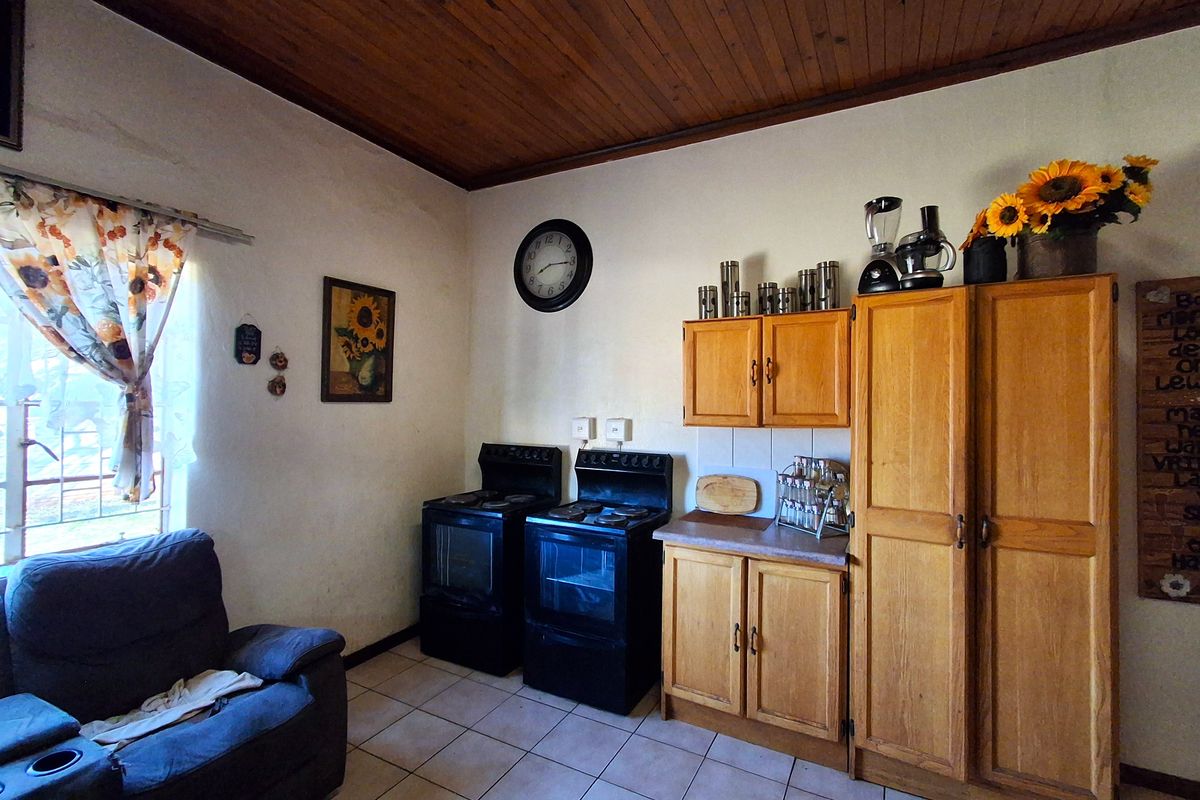 A dated kitchen featuring timber ceilings, tiled flooring, wooden cabinetry, and dual freestanding electric stoves.