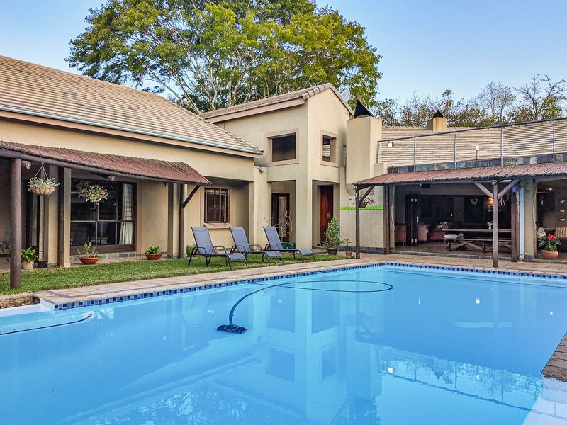 Spacious outdoor entertainment area featuring a large swimming pool, covered patio spaces, and a balcony overlooking the garden.