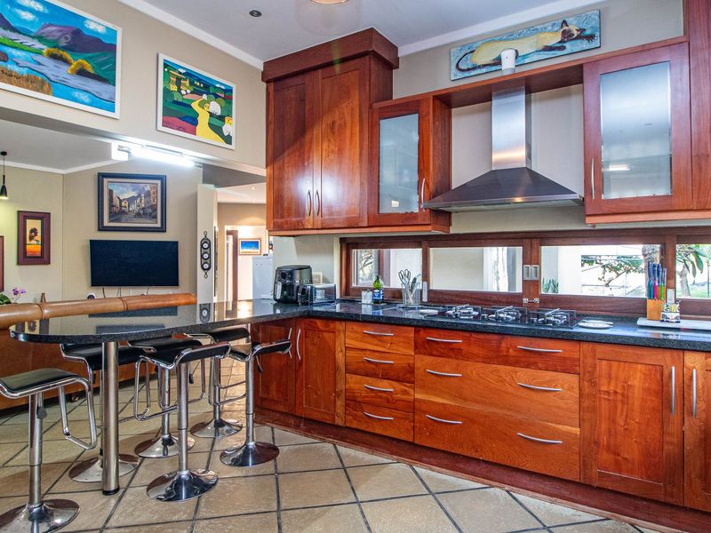 Open plan kitchen featuring warm wooden cabinetry, granite countertops, a gas hob with extractor fan, and a breakfast bar overlooking the living area.
