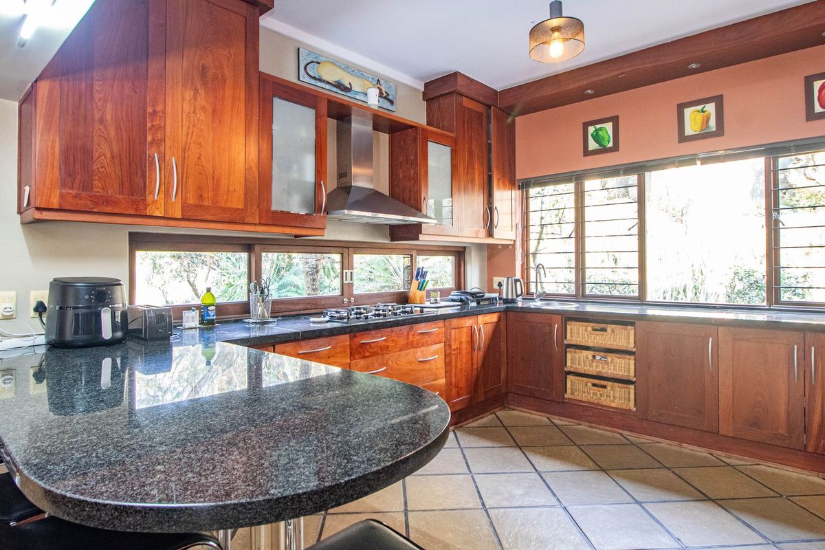 A functional kitchen featuring warm wooden cabinetry, granite countertops, a gas hob with extractor fan, and tiled flooring with ample natural light.