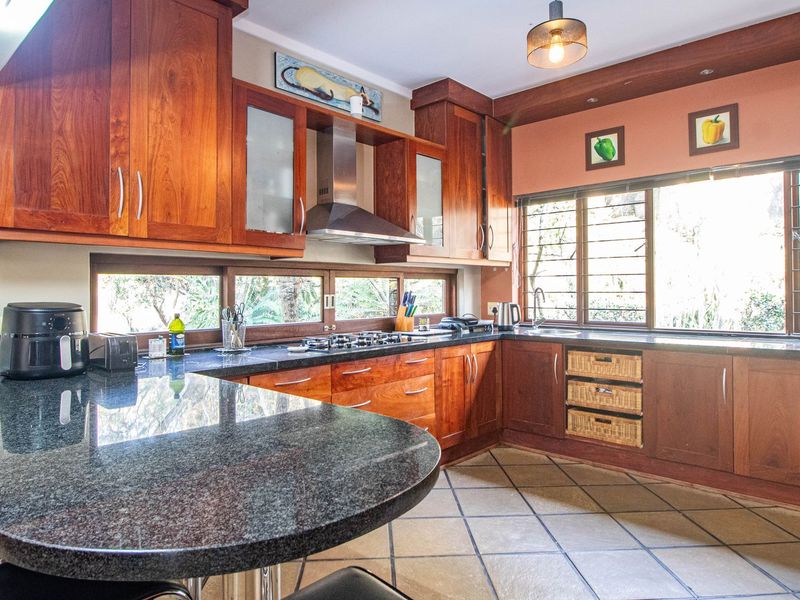 A functional kitchen featuring warm wooden cabinetry, granite countertops, a gas hob with extractor fan, and tiled flooring with ample natural light.