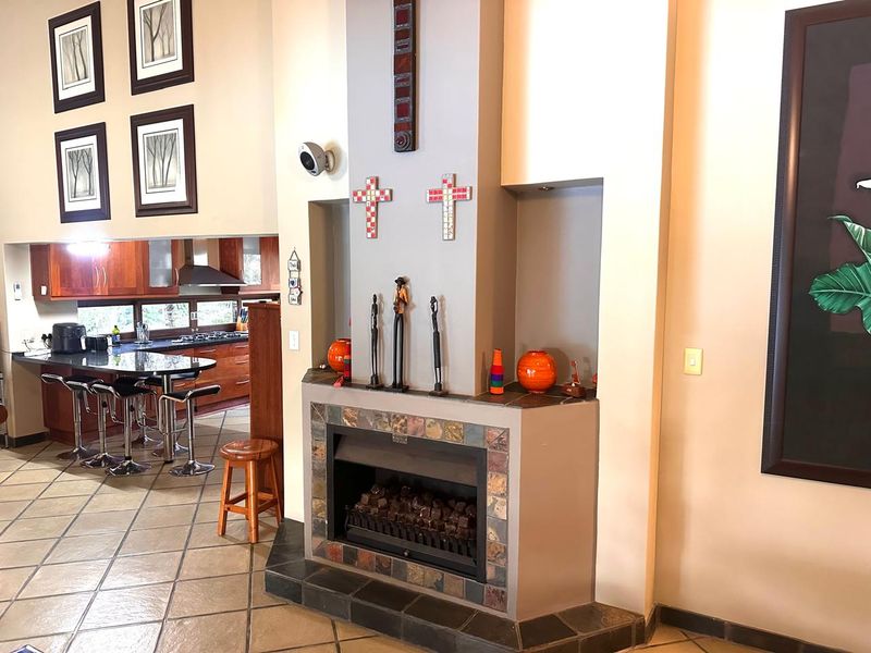 Open plan living area featuring a central fireplace with stone tile detailing, flowing into a kitchen with wooden cabinetry and a breakfast island.