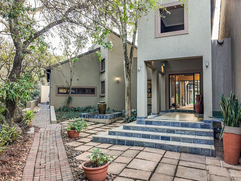 A well-maintained front entrance featuring stone-paved patio, tiered steps, a decorative water feature, and a brick pathway leading to the main residence.