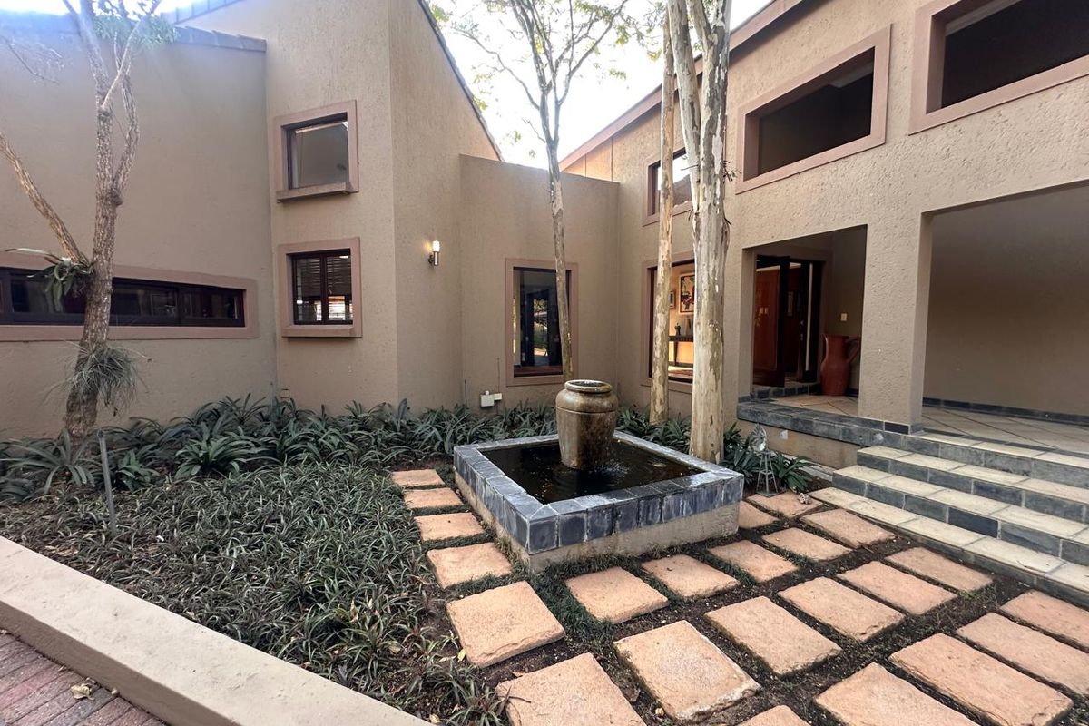 A tranquil rear courtyard featuring a central stone water feature, paved walkways, and landscaped garden beds set against the home's exterior facade.