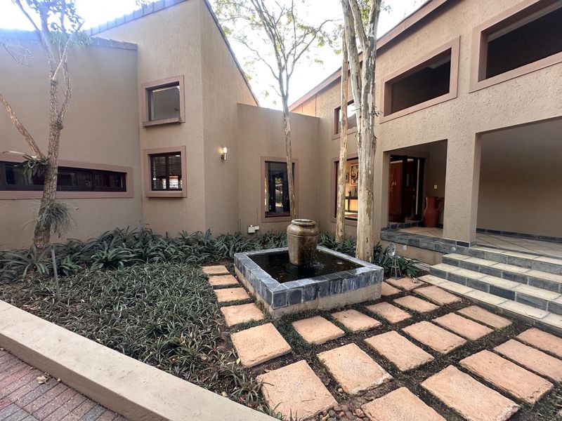 A tranquil rear courtyard featuring a central stone water feature, paved walkways, and landscaped garden beds set against the home's exterior facade.