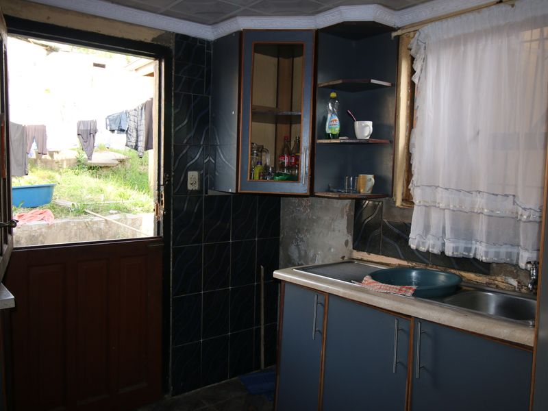 A small kitchen area featuring dark cabinetry, a stainless steel sink, and direct access to the rear exterior.