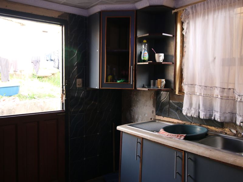 A small kitchen area featuring built-in cabinetry and a stainless steel sink, with direct access to the exterior. The space requires significant cosmetic renovation.