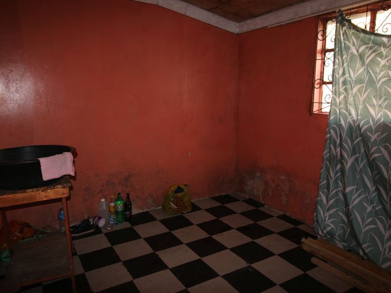 A utility space featuring checkered floor tiles, security bars on the window, and walls showing significant signs of damp and surface deterioration.