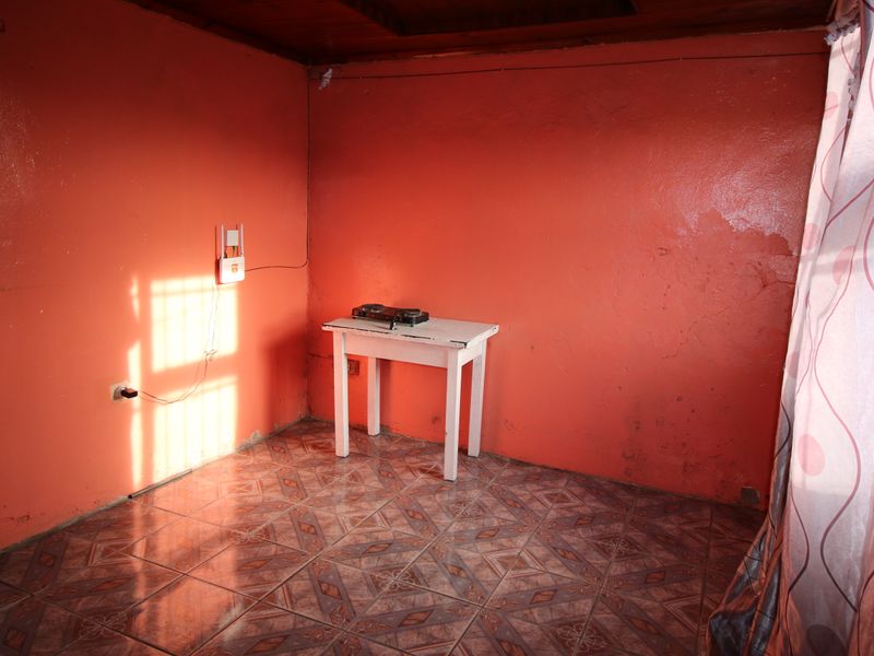 A vacant living area featuring tiled flooring and a timber ceiling, currently requiring cosmetic updates and wall repairs.