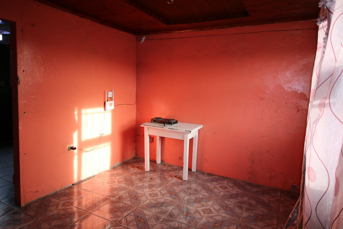 A sparsely furnished room featuring timber ceiling panels and patterned ceramic floor tiles, requiring cosmetic updates to improve the overall aesthetic.