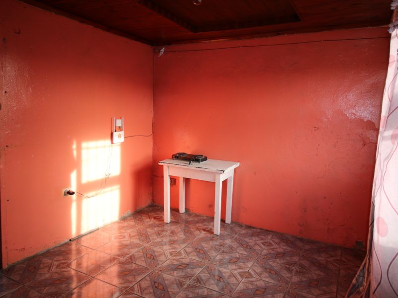 A sparsely furnished room featuring timber ceiling panels and patterned ceramic floor tiles, requiring cosmetic updates to improve the overall aesthetic.
