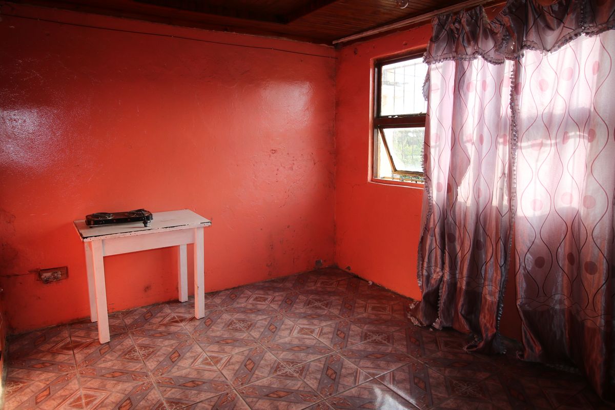 A vacant bedroom featuring tiled flooring, a timber ceiling, and a window with security bars, requiring cosmetic updates to the wall finishes.