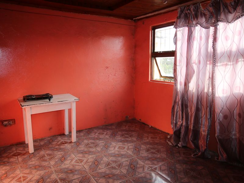 A vacant bedroom featuring tiled flooring, a timber ceiling, and a window with security bars, requiring cosmetic updates to the wall finishes.