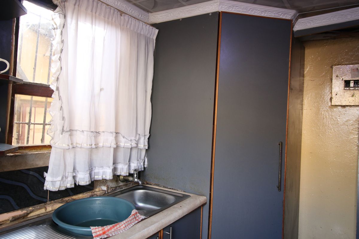 A dated kitchen area featuring a stainless steel sink, built-in cabinetry, and laminate countertops, showing significant signs of wear and required maintenance.