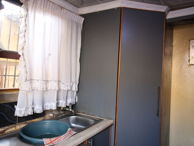 A dated kitchen area featuring a stainless steel sink, built-in cabinetry, and laminate countertops, showing significant signs of wear and required maintenance.