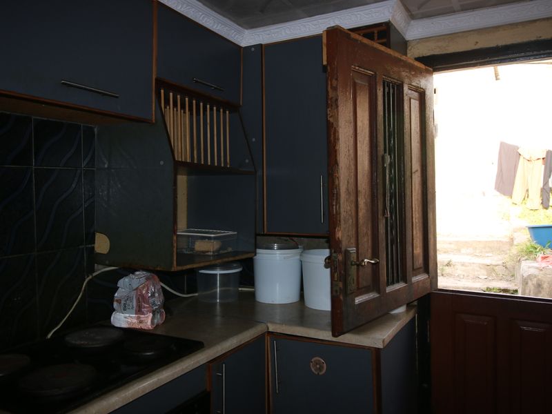 A compact kitchen featuring dark cabinetry, a tiled splashback, and an electric hob, with direct access to an outdoor area.
