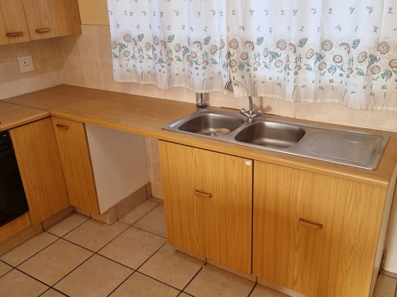 A functional kitchen featuring wood-look laminate cabinetry, a stainless steel double sink, built-in oven, and ceramic hob with tiled flooring and backsplash.