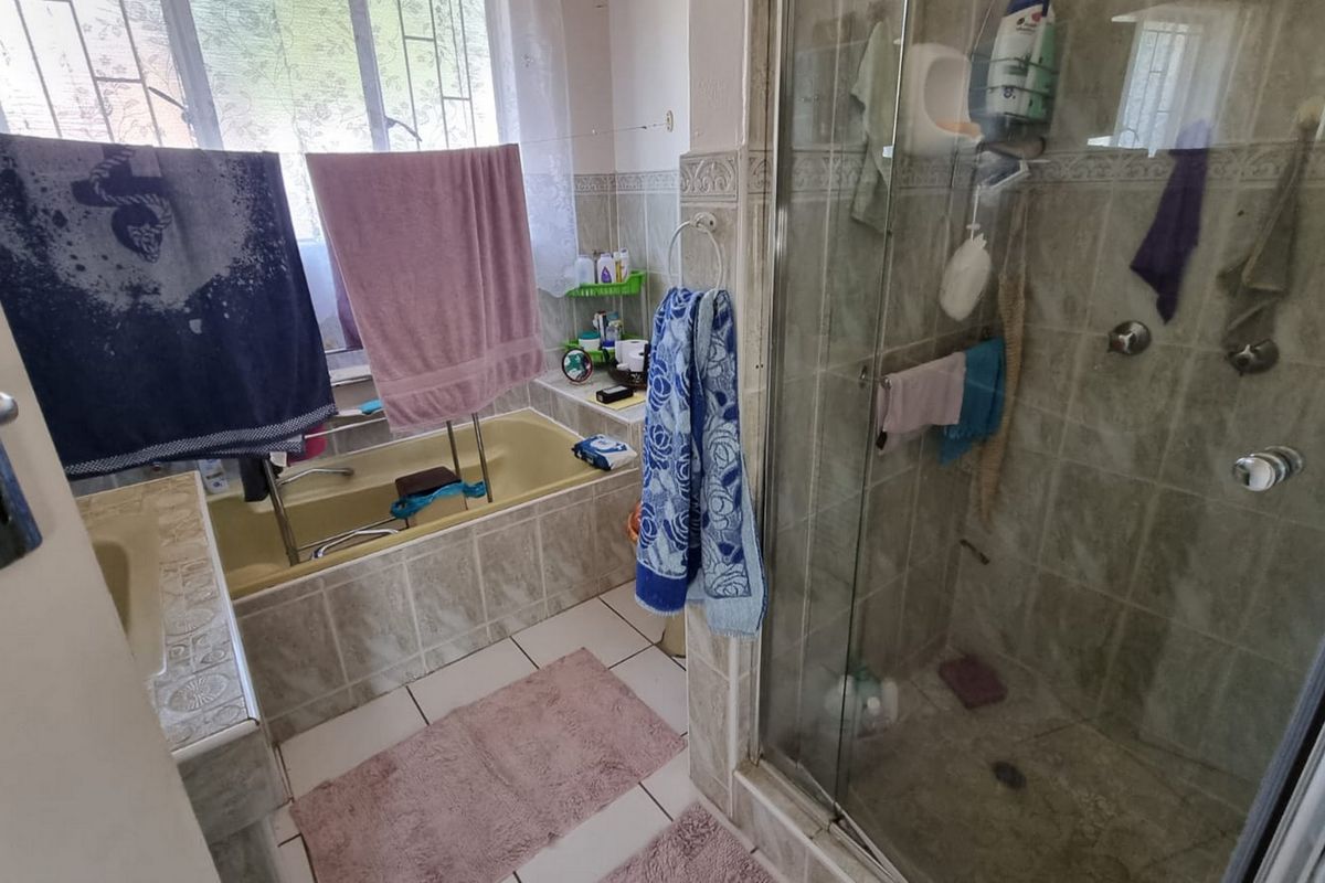 A functional bathroom featuring a built-in bathtub, a separate glass-enclosed shower, and tiled finishes throughout.