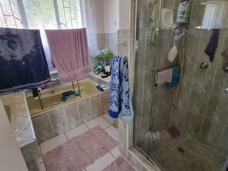 A functional bathroom featuring a built-in bathtub, a separate glass-enclosed shower, and tiled finishes throughout.