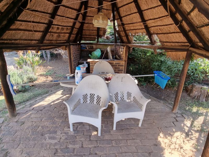 Outdoor thatched lapa area featuring brick paving and a built-in brick braai, providing a rustic entertainment space in the garden.