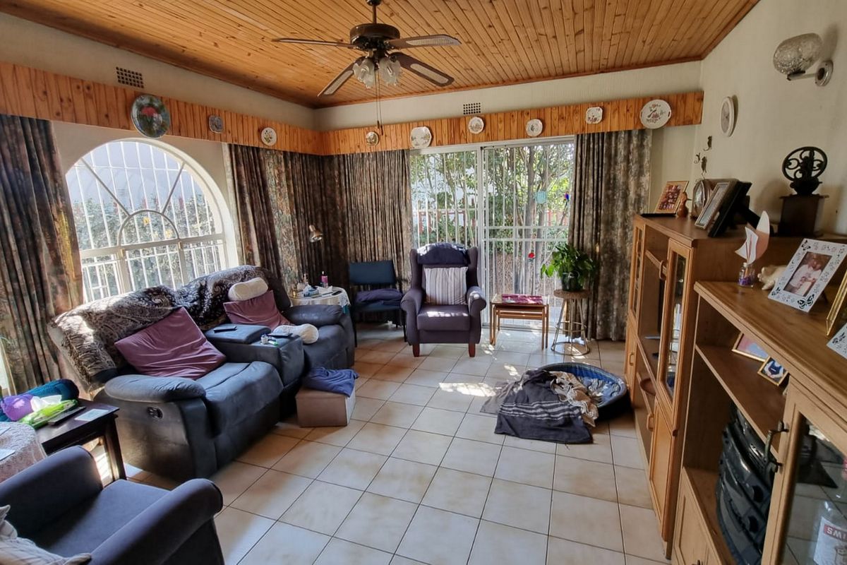 A living room featuring a timber tongue and groove ceiling, ceramic tiled flooring, and access to the garden through a sliding glass door.