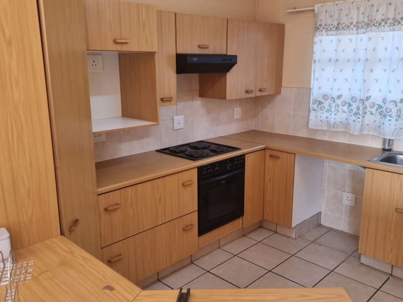 Functional kitchen featuring wood-look laminate cabinetry, built-in oven with electric hob, extractor fan, and a double bowl sink with tiled backsplash.