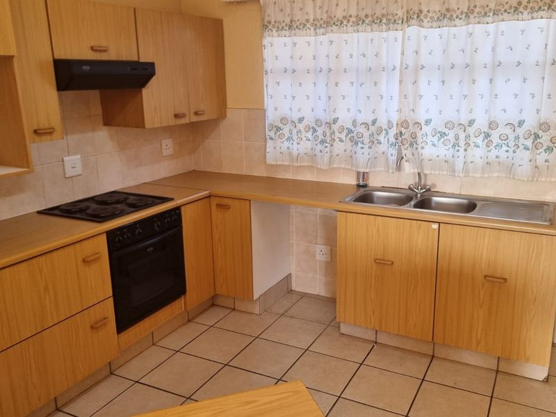 A functional kitchen featuring light wood-tone cabinetry, laminate countertops, a built-in oven with hob, and a double stainless steel sink with tiled backsplash.