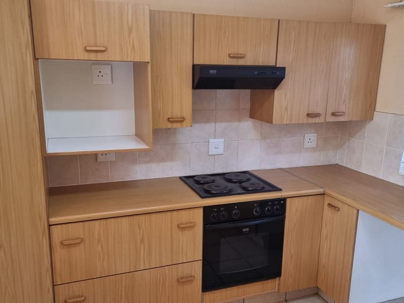 A functional kitchen featuring wood-look laminate cabinetry, built-in oven, electric hob, extractor fan, and tiled splashback.