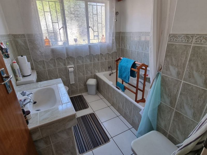 A functional bathroom featuring a tiled vanity, built-in bathtub with shower mixer, and tiled wall finishes.