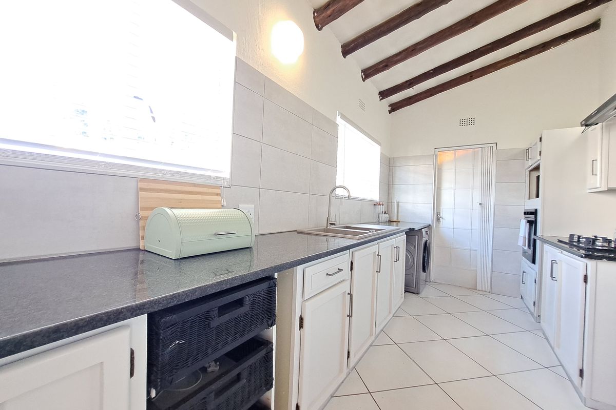Kitchen featuring exposed timber ceiling beams, granite countertops, built-in oven, gas hob, and tiled flooring with ample storage cabinetry.