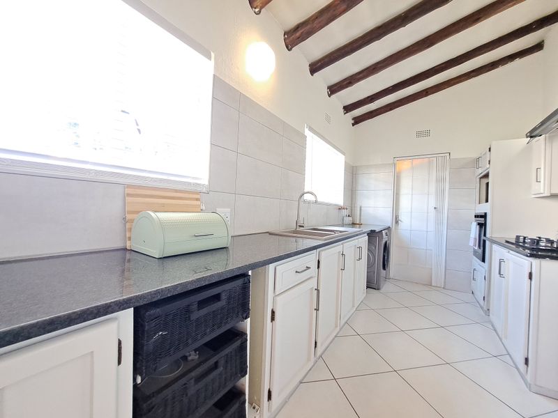 Kitchen featuring exposed timber ceiling beams, granite countertops, built-in oven, gas hob, and tiled flooring with ample storage cabinetry.
