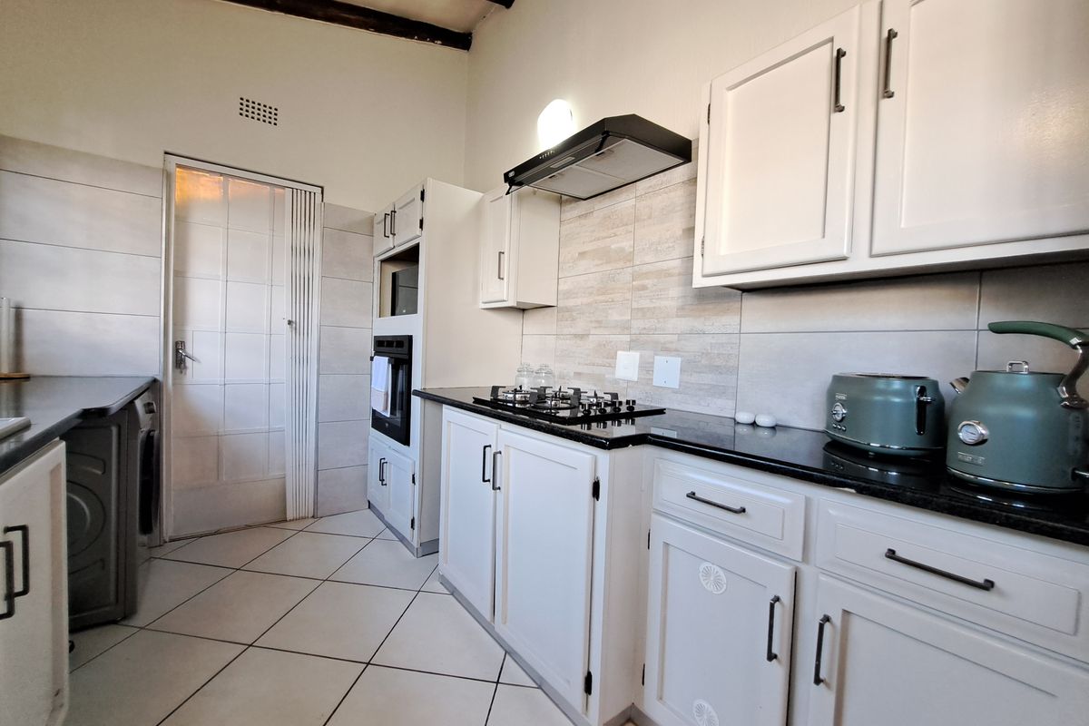 A well-maintained kitchen featuring white cabinetry, granite countertops, a gas hob with extractor fan, built-in oven, and tiled flooring with exposed ceiling beams.