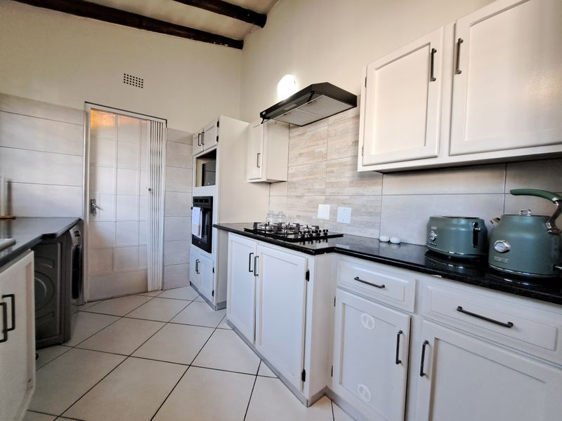 A well-maintained kitchen featuring white cabinetry, granite countertops, a gas hob with extractor fan, built-in oven, and tiled flooring with exposed ceiling beams.