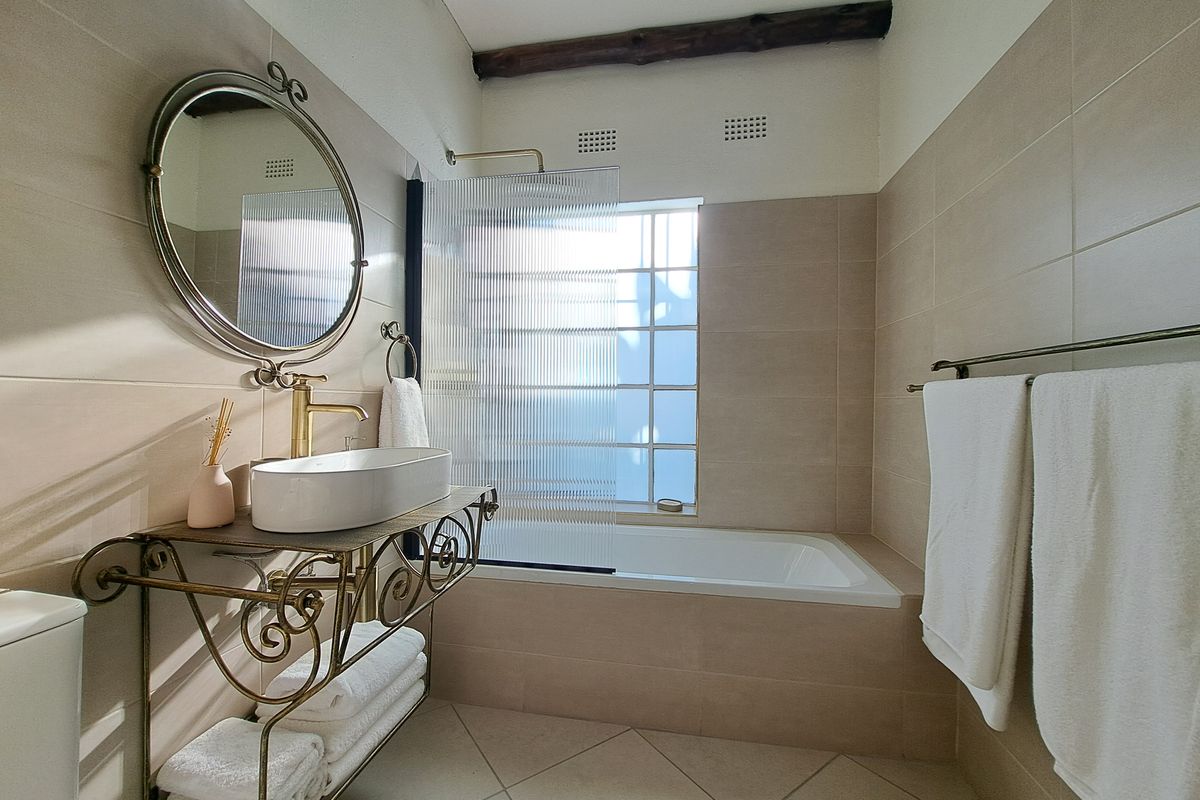A well-maintained bathroom featuring a vessel sink with brass fixtures, a built-in bathtub with a fluted glass screen, and rustic exposed timber ceiling beams.