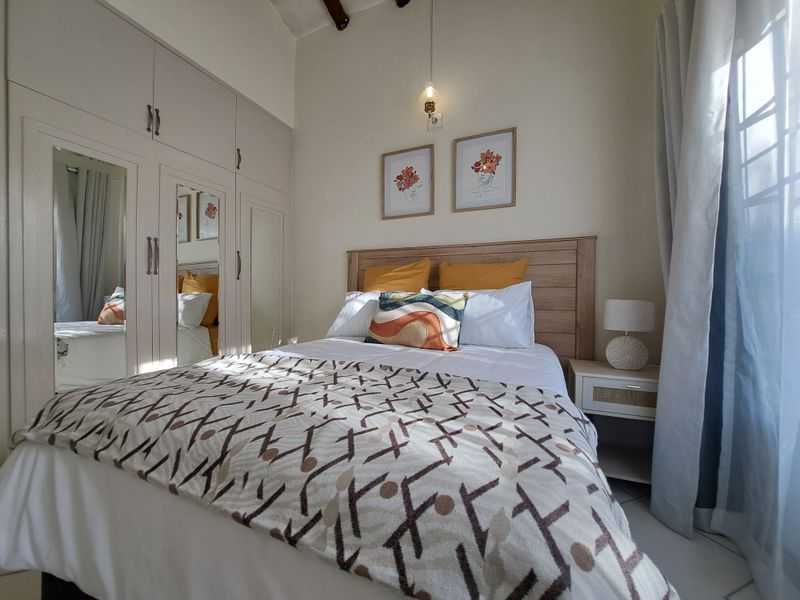 A well-maintained bedroom featuring built-in cupboards with mirrored doors and exposed ceiling beams, creating a bright and functional living space.